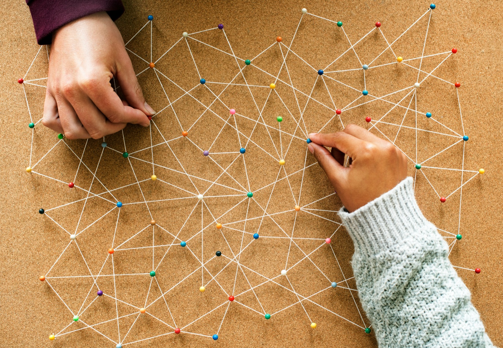 Hands connecting pins with string, representing Flown's connected market knowledge graph